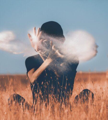 man sitting on brown grass field playing with smoke