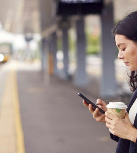 Businesswoman Waiting On Train Platform With Wireless Earbuds Listens To Music On Mobile Phone
