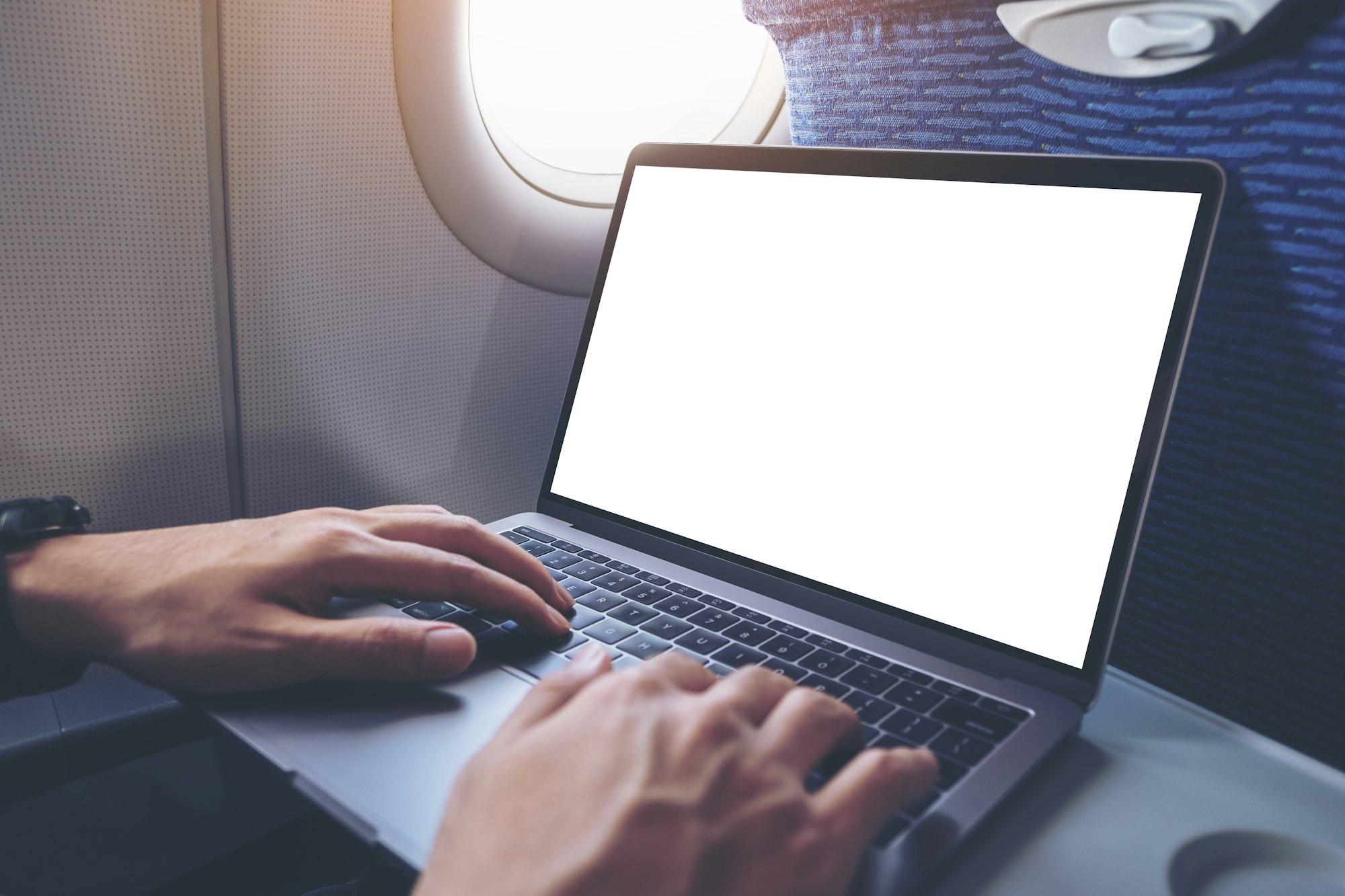A man using and typing at laptop computer with blank white desktop screen in the cabin